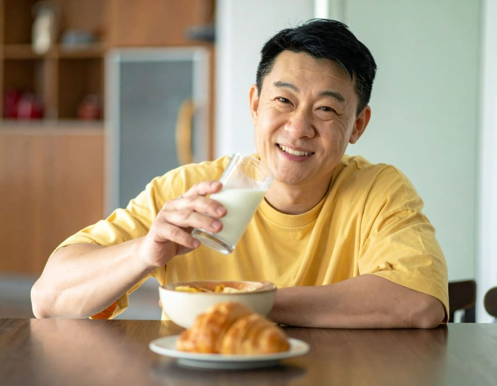 亞洲人男子在餐桌上喝牛奶搭配早餐